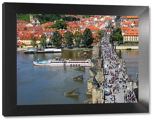 Tourists walking over the Charles Bridge over the Vltava River with a boat sailig