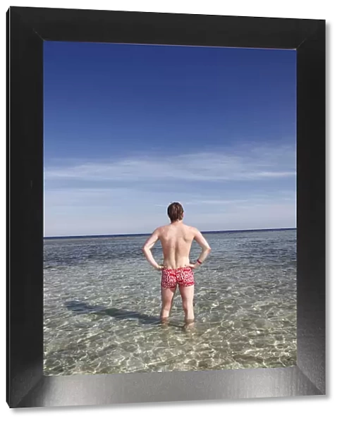 Rear view of a man on summer holiday standing in the sea on the beach
