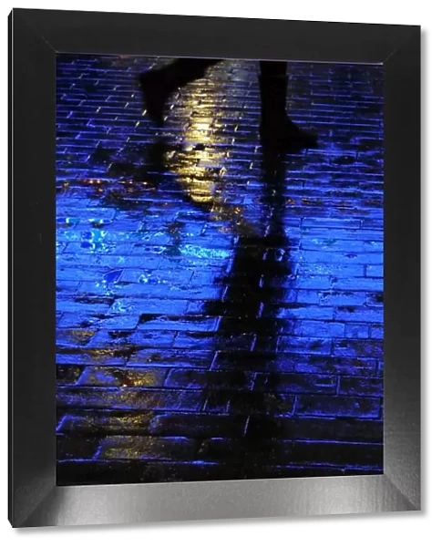 Blue light shining on a wet brick paved pavement surface with shadow of a person walking by