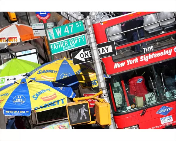 Busy street scene with red tourist sightseeing bus, street signs, and fast food stall umbrellas, New York. America