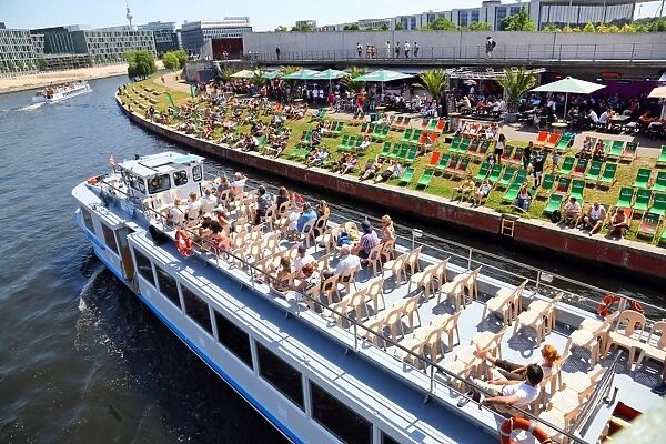 Artificial beach with deckchairs beside the River Spree with a tourist sightseeing boat in Berlin, Germany
