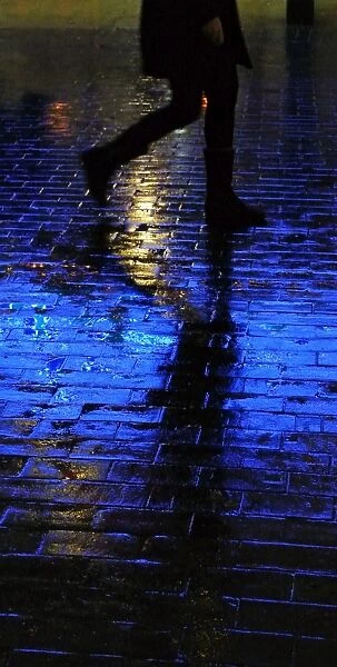Blue light shining on a wet brick paved pavement surface with shadow of a person walking by