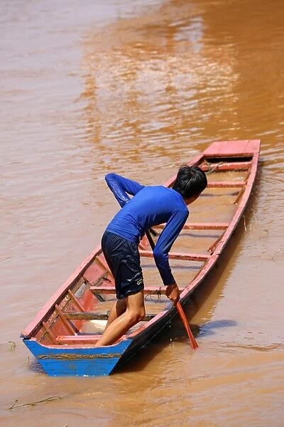 Boy paddling a flooded sinking boat on the Mekong River in Luang Prabang, Laos