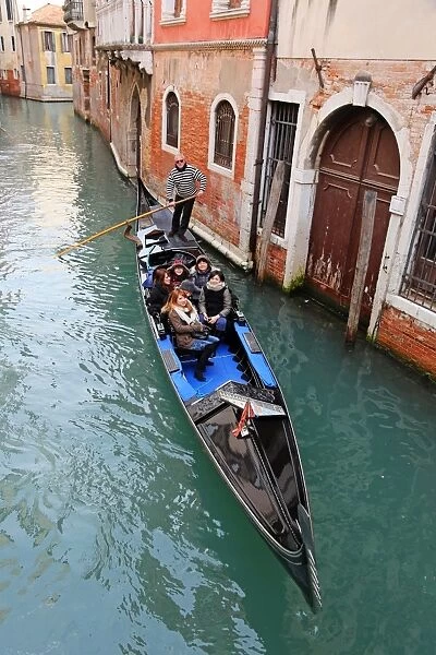 Gondoleer poling a gondola carrying tourists along a canal, in Venice, Italy