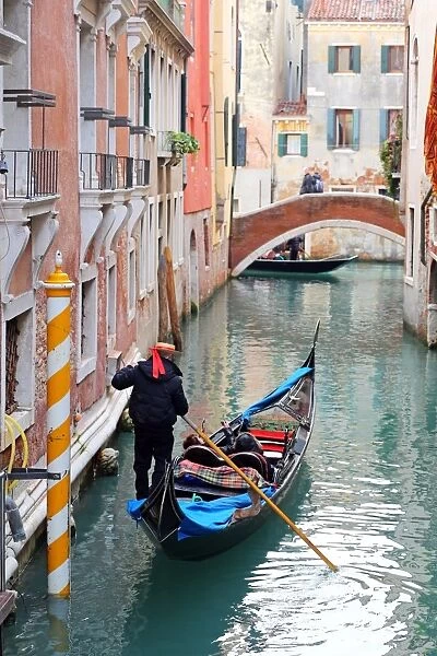 Gondoleer poling a gondola carrying tourists along a canal, in Venice, Italy
