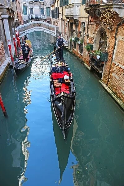 Gondoleers poling gondolas carrying tourists along a canal, in Venice, Italy