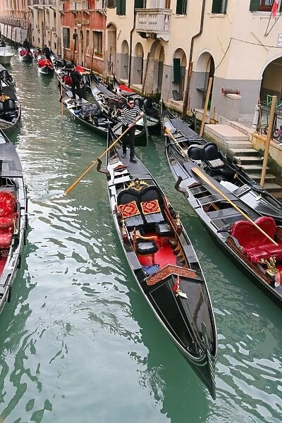 Gondoleers poling gondolas carrying tourists along a canal, in Venice, Italy