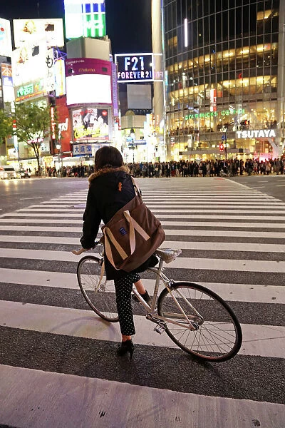 Japanese street scene showing crowds of people crossing the street and a cyclist on a pedestrian crossing in Shibuya, Tokyo, Japan