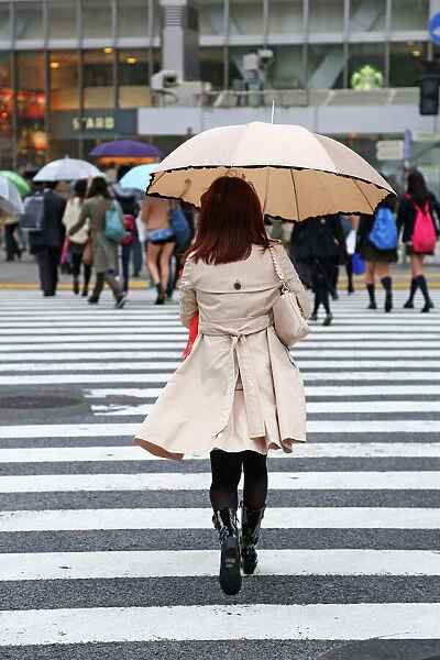 Japanese woman crossing the street with umbrella in the rain on a pedestrian crossing in Shibuya, Tokyo, Japan
