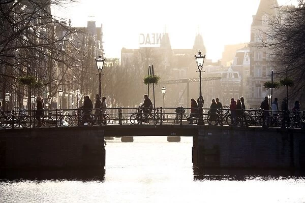 Silhouette of people and bicycles riding over a bridge over a canal in Amsterdam, Holland