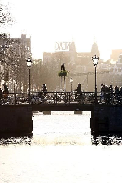Silhouette of people and bicycles riding over a bridge over a canal in Amsterdam, Holland