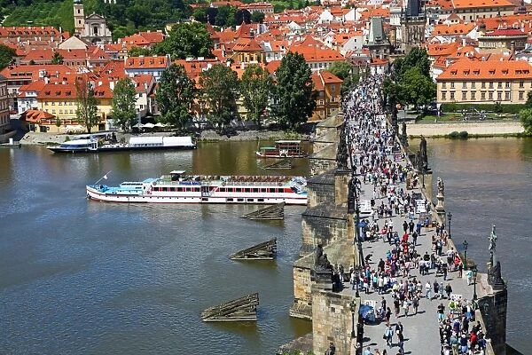 Tourists walking over the Charles Bridge over the Vltava River with a boat sailig
