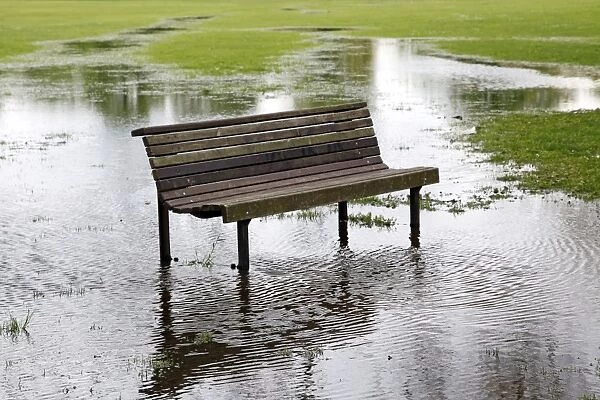 Empty wooden bench in flooded park with reflection in water