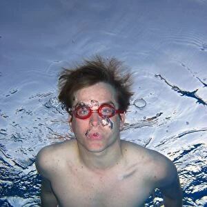 Man swimming underwater wearing goggles blowing bubbles