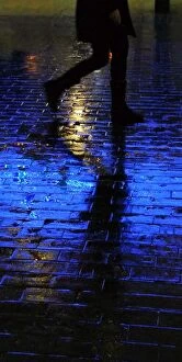 Perfect for Phone Covers Collection: Blue light shining on a wet brick paved pavement surface with shadow of a person walking by