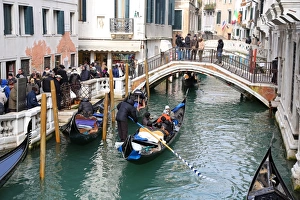 Gondoleers poling gondolas carrying tourists along a canal, in Venice, Italy