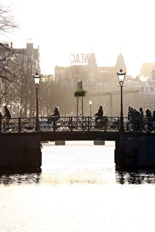 Silhouette of people and bicycles riding over a bridge over a canal in Amsterdam, Holland Silhouette of people and bicycles riding over a bridge over a canal in Amsterdam, Holland